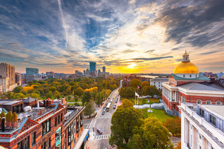 A wide shot of Boston with the state capitol in the foreground and a sunset reflecting off the clouds.